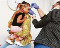  ??  ?? Berens checks the head size of 18-month-old Sereen Wheeler as she’s comforted by her mother, Aziza Awed.