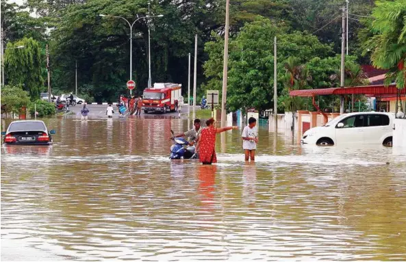  ??  ?? Water world: Lim Garden residents braving their way through knee-deep waters after the downpour in Ipoh yesterday.