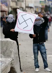  ?? (Reuters) ?? PALESTINIA­NS HOLD a sign depicting a swastika during clashes at Kalandiya checkpoint on the road to Jerusalem in 2010.