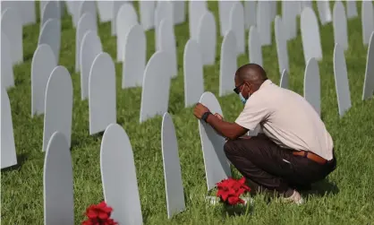  ??  ?? Quincy Cohen writes the name of a friend lost to Covid-19 on to a tombstone at a memorial for local lives lost in North Miami, Florida. Photograph: Joe Raedle/Getty Images