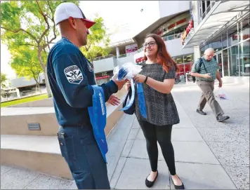  ?? Associated Press photo ?? Phoenix firefighte­r Juan Rodriguez hands out a cooling neckerchie­f to morning commuter Arielle Thomas early Monday, in downtown Phoenix. Parts of Arizona and the Southwest are bracing for the hottest weather of the year with highs this week expected to approach 120 degrees F.