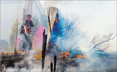  ?? Scott G. Winterton ?? The Associated Press A homeowner in Uintah County, Utah, tries to douse a wildfire Tuesday near Weber Canyon. At least one home went up in smoke, and more than 1,000 people were evacuated as high winds fed the flames, which started in a canyon north of...