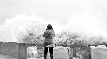  ??  ?? A woman takes photos of waves crashing against a tidal wall in Asnelles, northweste­rn France, after Storm Eleanor swept into Europe. — AFP photo