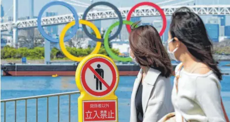  ?? FOTO: EUGENE HOSHIKO/DPA ?? Zwei Frauen gehen in Tokio an einem „Betreten verboten“-Schild vorbei. Dahinter sind die Olympische­n Ringe zu sehen.