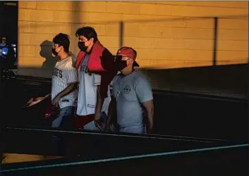  ?? Gina Ferazzi Los Angeles Times ?? ANGELS FANS wear masks as they walk through the last rays of sunlight at Angel Stadium. With capacity limited, some fans joked about the easy parking, while others were simply happy to wear Angels’ gear again.