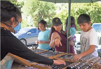  ??  ?? Maxentia Williams, owner of Created by Navajo Hands, left, assists Phranchesc­a Phillip, 27, with her children, Tatianna Lundy, 10, left, Paityn Phillip, 2, and Jerimiah Phillip,12, of Flagstaff, at a Navajo craft market off 89A in Sedona.