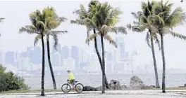  ?? LYNNE SLADKY/AP ?? The Miami skyline is shrouded in clouds as a cyclist rides along Biscayne Bay on Friday. A trough of low pressure moving through the Florida Straits could organize over the northwest Bahamas on Saturday and become the first named storm of the hurricane season.