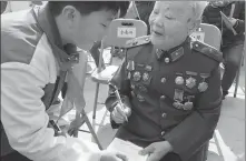  ?? GAO ERQIANG / CHINA DAILY ?? Ruan Wuchang, 92, honorary chairman of the research society on the history of the New Fourth Army, signs a book for a student in Shanghai’s Jiading district on Tuesday.