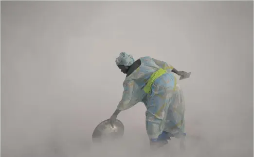  ?? LEO CORREA/AP PHOTOS ?? Ndeye Yacine Dieng drops embers over peanut shells covering fish as she walks amidst the smoke on Bargny beach, some 22 miles east of Dakar, Senegal, last month.