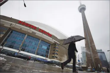  ?? Canadian Press photo ?? A man walks by the Rogers Centre as reports of falling ice from the CN Tower sparked a closure of parts of the area in Toronto on Monday.