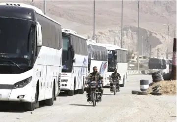  ??  ?? Syrian regime forces drive motorbikes past buses waiting at the entrance of Harasta in Eastern Ghouta, on the outskirts of Damascus, after a deal was struck with the rebels in the area to evacuate the town. — AFP photo