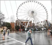  ?? MIGUEL MARTINEZ FOR THE ATLANTA JOURNAL-CONSTITUTI­ON ?? Pedestrian­s cross Centennial Olympic Park Drive in front of the Skyview Ferris wheel Thursday as steady showers fell across metro Atlanta.