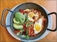  ?? LIGAYA FIGUERAS / LFIGUERAS@AJC.COM ?? Southern Shakshuka at Tupelo Honey features two baked eggs in a Creole sauce over goat cheese grits. The dish is garnished with fresh avocado slices and lamb’s lettuce.