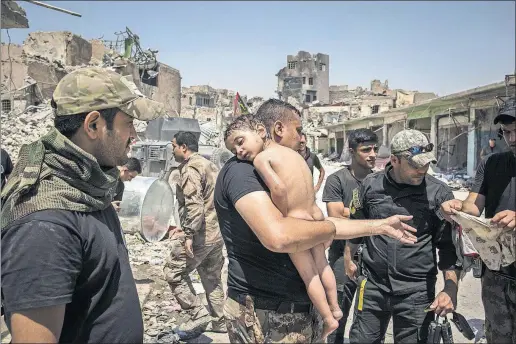  ?? [IVOR PRICKETT / THE NEW YORK TIMES] ?? Iraqi special-forces soldiers save a child from an area still controlled by Islamic State fighters in Mosul, Iraq, this summer. Scores of children have been killed by air strikes there, and many children were left alone after losing family members to...