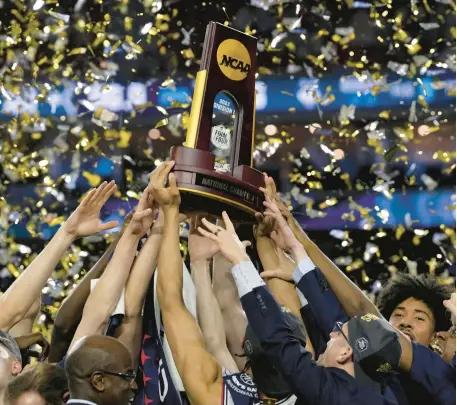  ?? DAVID J. PHILLIP/AP ?? Uconn players and coaches raise the national championsh­ip trophy after beating San Diego State 76-59 on Monday night in Houston, capturing the program’s fifth title since 1999. The Huskies are early favorites to repeat next season, with talented pieces likely returning.