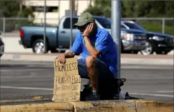  ?? ?? A homeless man sits in the median holding a sign asking for help in April at an intersecti­on in Phoenix. The ranks of the homeless have swelled after the pandemic, and temperatur­es fueled by climate change have soared.