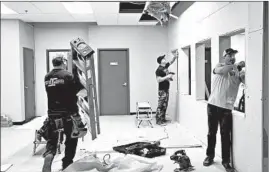  ?? STACEY WESCOTT/CHICAGO TRIBUNE ?? Luis Vargas, left, carries a ladder while Geoffrey Sands, center, and Corey Kelly build customer checkout windows at EarthMed medical cannabis dispensary in Addison on Dec. 13.