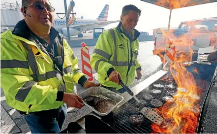  ?? AP ?? Airport operation workers wearing fluorescen­t safety jackets flipped burgers and hot dogs on a grill set up on the tarmac in front of a plane at Salt Lake City Internatio­nal Airport. Airport officials treated workers from the TSA, FAA and Customs and Border Protection to a free barbecue lunch as a gesture to keep their spirits up during the shutdown.