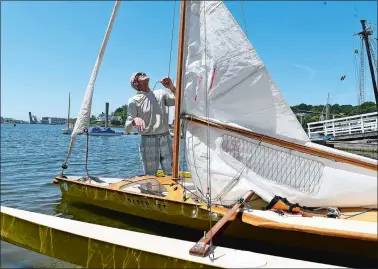  ?? SARAH GORDON/THE DAY ?? Dudley Dix, of Virginia Beach, raises the sail of Paper Jet, a wood skiff, on Sunday as he prepares to sail on the Mystic River during the 30th annual WoodenBoat Show at the Mystic Seaport Museum. This was the prototype made by Dix, a boat designer and builder who was also a vendor at the event, about 50 years ago. Since then he estimates he has made or sold plans for at least 100 more of the boats.