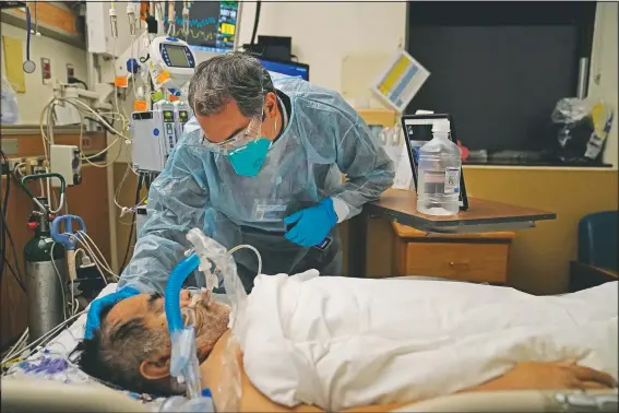  ?? (AP/Jae C. Hong) ?? Chaplain Kevin Deegan places his hand on the head of a covid-19 patient while praying for him at Providence Holy Cross Medical Center in the Mission Hills section of Los Angeles on Jan. 9. Deegan’s job, and that of his fellow chaplains at the 377-bed medical center, is to minister to every one of them and also their loved ones. So each day for the past 11 months he has been entering the rooms of the sick and dying clad in a face mask, face shield, gloves and full body cover to pray with them, hold their hands, gently brush their foreheads and reassure them there is nothing to fear.