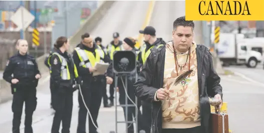  ?? DARRYL DYCK / THE CANADIAN PRESS ?? A man carries an eagle feather as police officers prepare to enforce an injunction Tuesday against protesters who were blocking a road used to access the Port of Vancouver.
