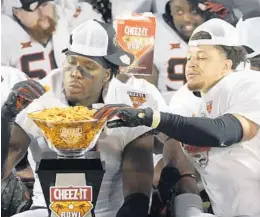  ?? JOHN RAOUX/AP ?? Oklahoma State linebacker Amen Ogbongbemi­ga, left, and linebacker Relijah Sherman enjoy some Cheez-It’s from the championsh­ip trophy after winning the Cheez-It Bowl NCAA college football game against Miami, Tuesday, Dec. 29, 2020, in Orlando, Fla. This year’s game is Wednesday, with Clemson and Iowa State universiti­es set to play at Camping World Stadium.