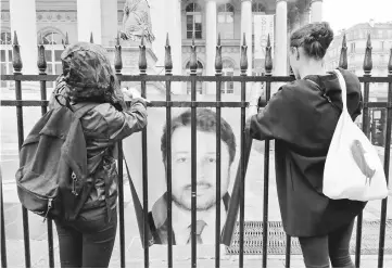  ?? — AFP photo ?? Two persons hang a portrait of Kilic on the fence of the historic French stock market building ‘Palais Brongniart’ in Paris.