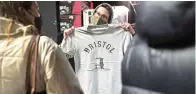  ?? PA via The Associated Press ?? ■ A person inside Rough Trade in Bristol, England, on Saturday holds up a T-shirt designed by street artist Banksy. The shirt is being sold to support four people facing trial accused of criminal damage in relation to the toppling of a statue of slave trader Edward Colston.