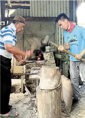  ?? ?? Learning the trade: master craftsman harun mahmud (left) showing abdul hakim the art of shaping the blade of a keris.