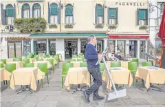  ??  ?? SLOW BUSINESS: A restaurant owner moves his menu in Venice on Thursday. The outbreak has hit hard in Italy, where tourism generates 13% of economic activity.