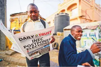  ?? AP ?? A man reads a newspaper which managed to print the news of the postponeme­nt in time in Kano, northern Nigeria, yesterday.