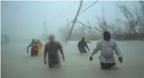  ?? AP PHOTO ?? Volunteers walk in the wind and rain Tuesday on a flooded road as they head to rescue families near the Causarina bridge in Freeport.