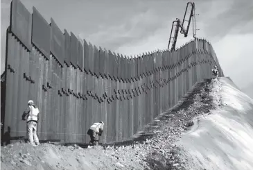  ?? MARIO TAMA Getty Images ?? A constructi­on crew works as new sections of the U.S.-Mexico border barrier are installed on Friday as seen from Tijuana, Mexico. President Donald Trump is holding off from a threatened national emergency declaratio­n to fund a border wall amidst the partial government shutdown, which has entered its third week, with little likelihood of it ending soon.