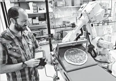  ?? JOSH EDELSON/FOR THE LOS ANGELES TIMES ?? Zume Pizza CTO Josh Goldberg controls a robot as it moves a pizza from a conveyor belt to an oven. One robot, top left, squirts a blob of sauce while another, top right, does the spreading, mimicking the movements of Zume’s head chef.