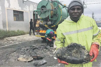  ?? Picture: Peter Luhanga ?? DOWN THE MANHOLE. Hamilton Mkhize holds one of the rocks he removed from a blocked sewer in Dunoon. Behind him is his colleague, Morris Ngadu.