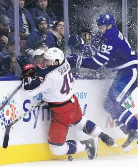  ?? COLE BURSTON / THE CANADIAN PRESS ?? Blue Jackets forward Lukas Sedlak and Leafs defenceman Igor Ozhiganov slam into the boards in Monday night’s game.