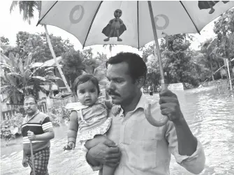  ?? Aijaz Rahi/AP ?? ■ A man holds a child as it rains after they were rescued from a flooded area Sunday in Chengannur in the southern state of Kerala, India. Some 800,000 people have been displaced and over 350 have died in the worst flooding in a century.