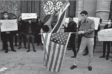  ?? VAHID SALEMI/AP ?? A day after the slaying of a top nuclear scientist, protesters prepare to burn American and Israeli flags Saturday in Tehran.