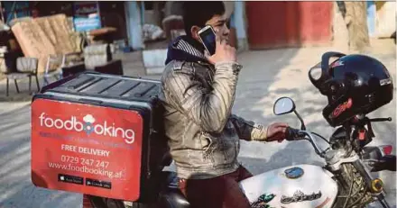  ?? AFP PIC ?? A courier for the Foodbookin­g online delivery service talking on the phone with a customer as he tries to find an address on a motorbike on a street in Kabul.