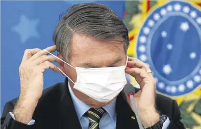  ?? REUTERS / ADRIANO MACHADO ?? Jair Bolsonaro trata de ponerse una mascarilla protectora.