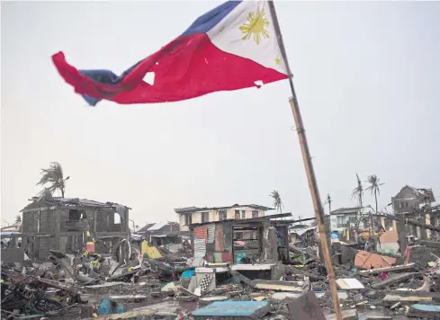  ??  ?? RAISING A RED FLAG: A flag of the Philippine­s flies over a destroyed neighbourh­ood in Tacloban, Philippine­s. The central Philippine city was ravaged by Typhoon Haiyan in November.