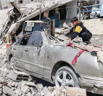  ?? — AFP ?? A boy clears rubble from atop a heavily damaged vehicle outside a destroyed building in Rafah.