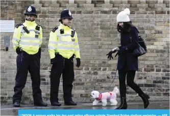  ?? — AFP ?? LONDON: A woman walks her dog past police officers outside Stamford Bridge stadium yesterday.