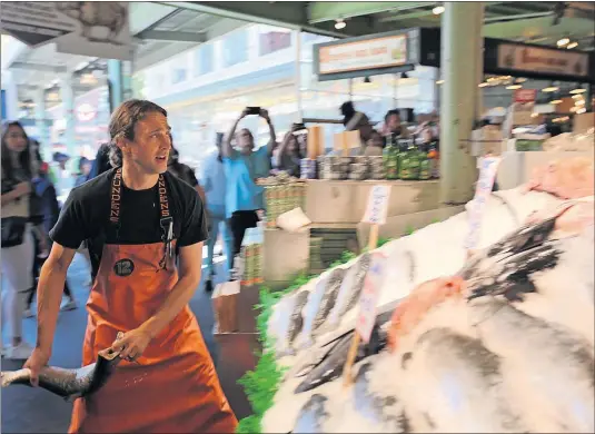  ?? [STEVE STEPHENS/DISPATCH PHOTOS] ?? A worker at Seattle's Pike Place Fish Market gets ready to heave a fish, a much-loved tradition.