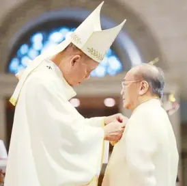  ?? ?? Manila Archbishop Jose Cardinal Advincula pins a gold medal featuring the images of Apostles Peter and Paul on Manuel V. Pangilinan at the Manila Cathedral on Wednesday.