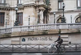  ?? Associated Press photo ?? A man rides his bicycle past by a graffiti reading “Macron equal to Louis 16” to reference to the king of France during the French Revolution in 1789 on the Paris Garnier Opera house in Paris, Sunday.