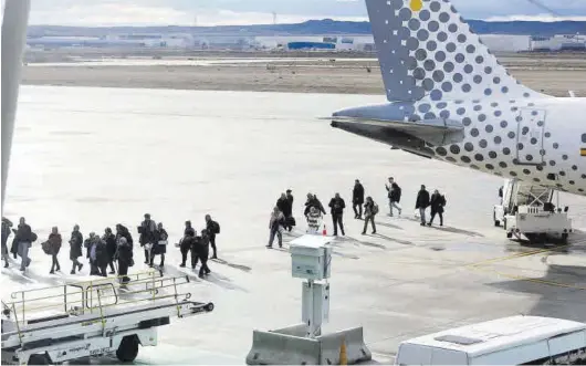  ?? MIGUEL ÁNGEL GRACIA ?? Un grupo de viajeros camina sobra la pista del Aeropuerto de Zaragoza.