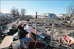  ?? MARK LENNIHAN/AP PHOTO ?? In this Nov. 14, 2012, photo, Louise McCarthy places an American flag on a street sign in the Breezy Point neighborho­od of Queens, N.Y. The sign survived a fire that swept through the seaside community during Superstorm Sandy two weeks earlier.