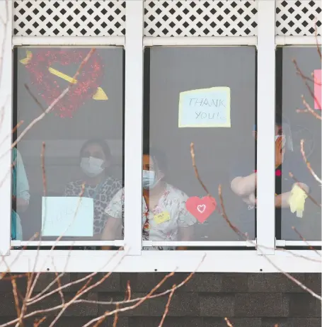  ?? BRENDAN MILLER ?? Health care workers stand in the windows at Mckenzie Towne Continuing Care Centre. The Alberta Union of Provincial Employees says it’s up to the province to ensure continuing-care employers provide top-up money to their workers after announcing the funding on April 20.