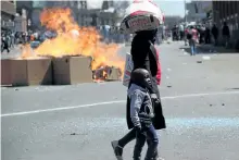  ?? AP PHOTO ?? A woman and child pass a fire set alight during a protest in Harare, Friday. The demonstrat­ion organised by opposition political parties calling for reforms, is the first time that the fractured opposition has joined forces in a single unified action...